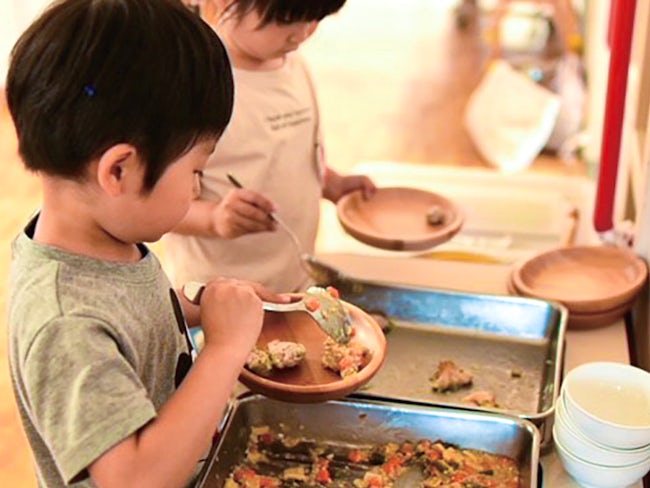 給食は、園内の「もりのキッチン」で作ります。味覚の発達する時期に本物の味を知ってもらうため、メニューは旬の食材を!友達と一緒に準備や後片づけをすることで、食事のマナーやルールを自然に身につけます。