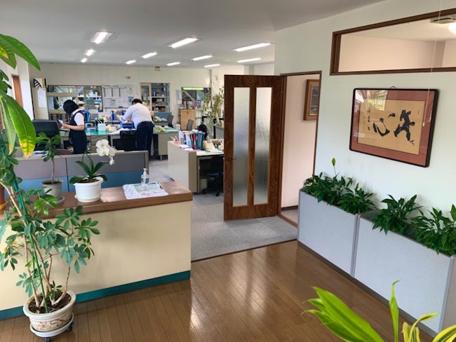事務所内風景。観葉植物を置いてたり、綺麗に整理整頓された広い事務所なので、働く上でのストレスはほぼないと思います。応接室の扉の向こう側に皆様のデスクがあります。