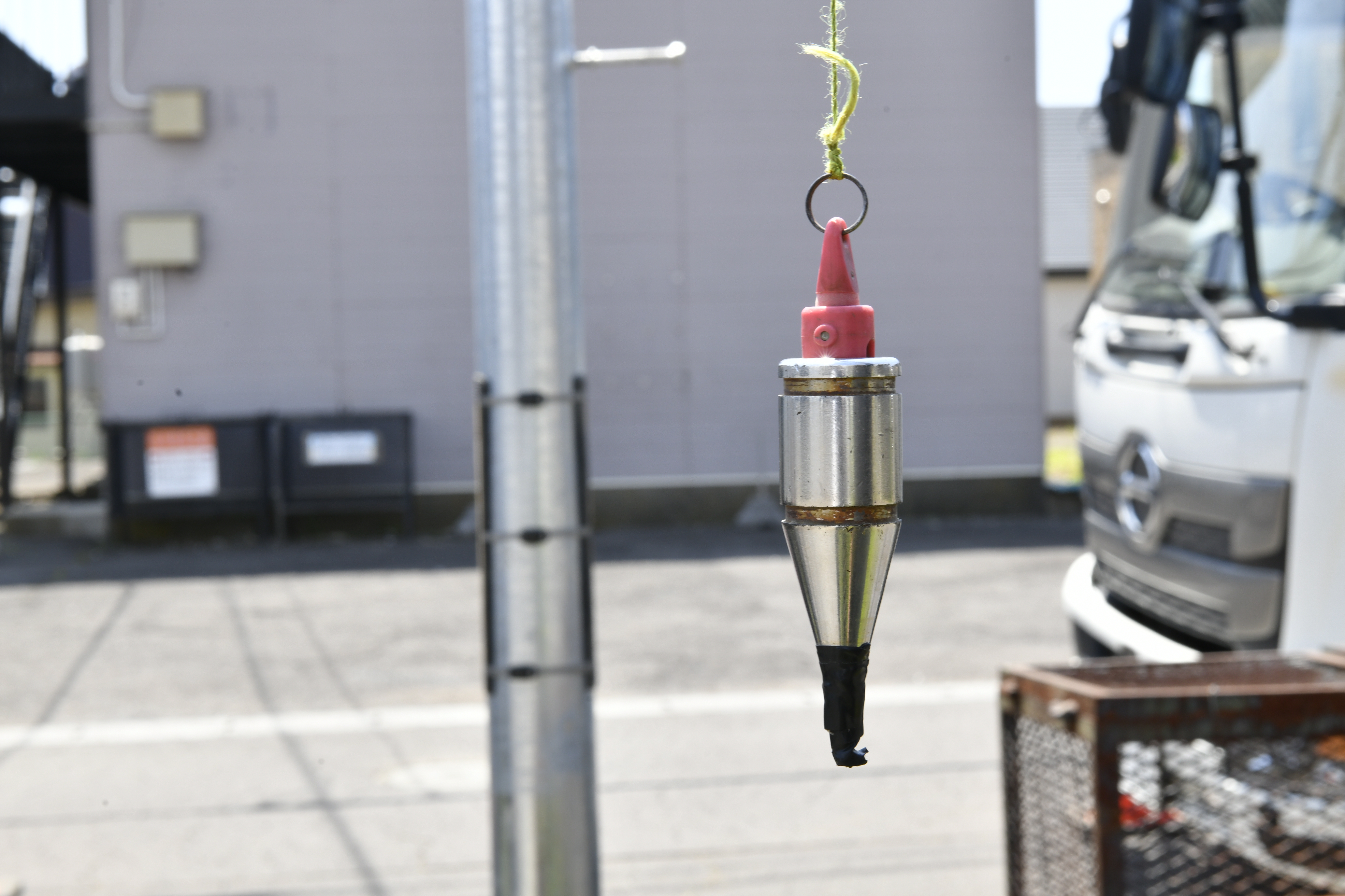 電柱を垂直に建てるために、傾きを計測する「下げ振り」という道具です。重力に従って糸が完全に真下を向く原理を利用します。現場ではこういったさまざま専用器具があります。