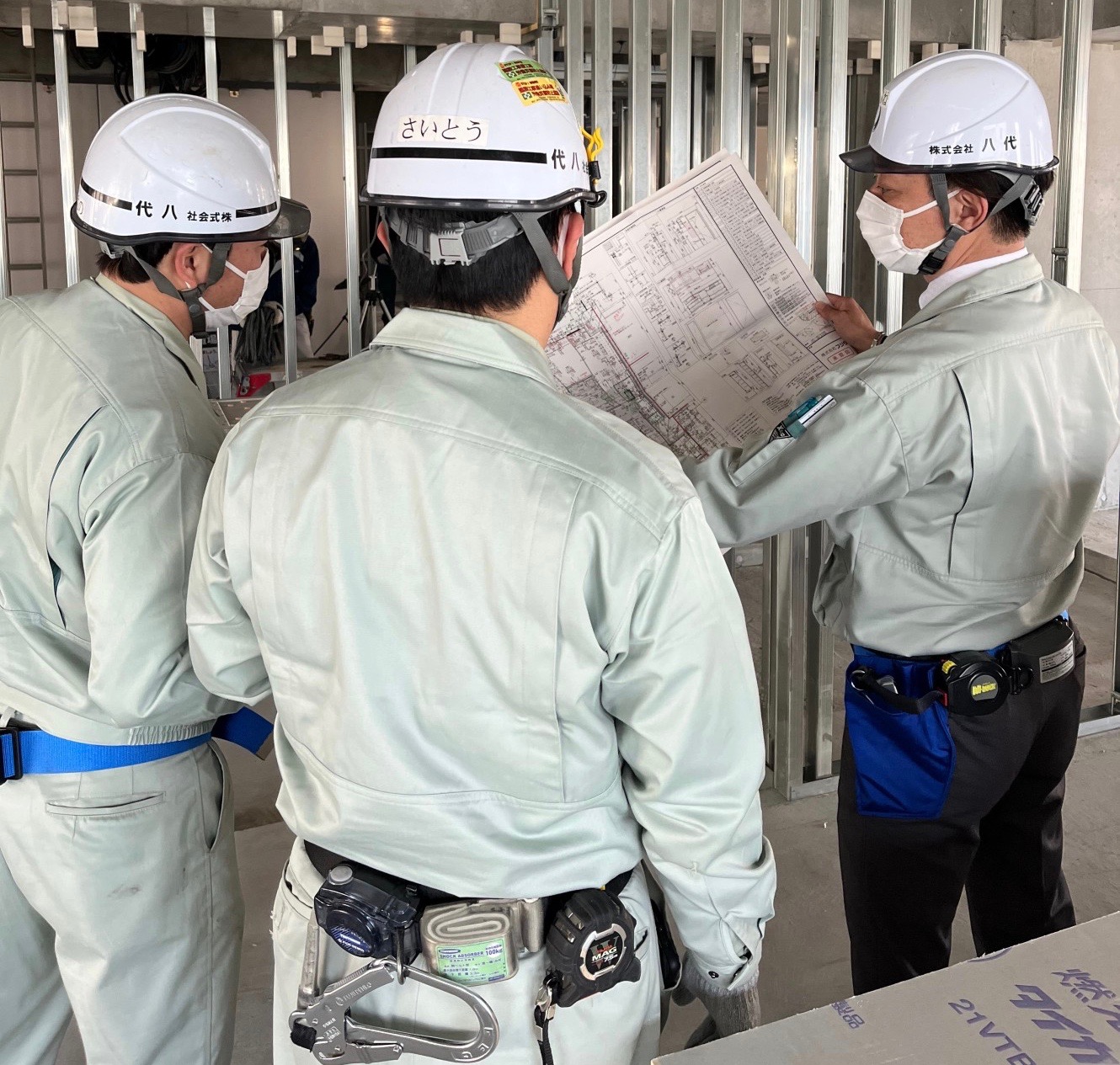 現場にて入社24年目40代次長のベテランスタッフ(図面を持っています)から指導を受けている様子。一人前になるまでは必ず先輩と同行し、一緒に案件を担当し、少しずつ作業フローを覚えてもらいます｡