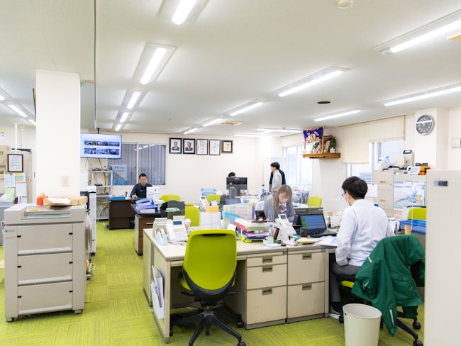 各製造棟の中心に、事務所の建物があります。緑と白が心地よい、明るいオフィス。仕切りがなく開放的な空間で、部署を越えた活発なコミュニケーションが生まれています。