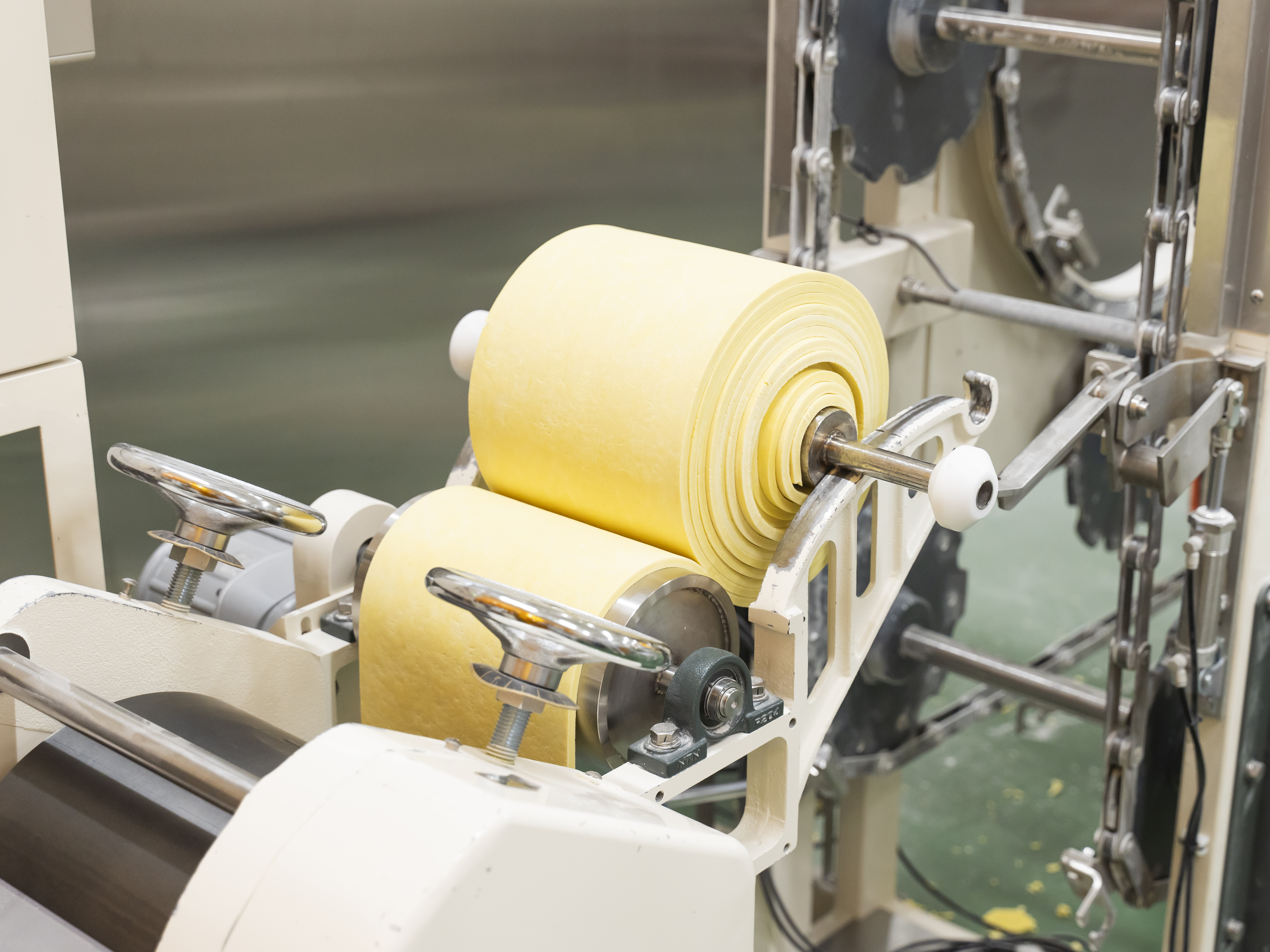 【基本的な製麺工程⑤】ミキシングで粒状になった麺生地をローラーで一度帯状にします。作業としてはシンプルですが、季節や時間帯によって最適な温度が異なるため、常に注意を払う必要があります。